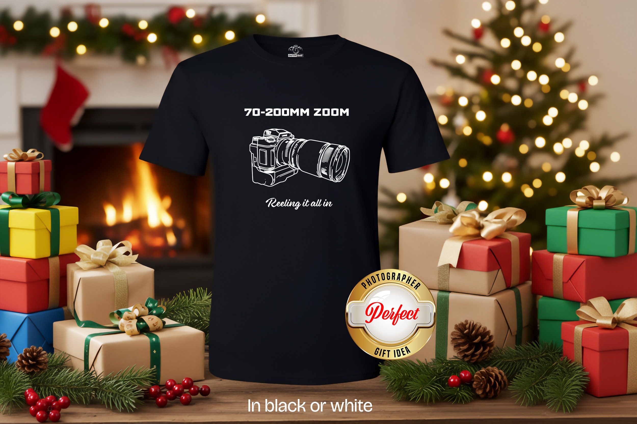 Black t-shirt with white technical drawing of camera with lens '70-200mm Zoom' above and 'Reeling it all in' below. This perfect gift is on a wood table surrounded by wrapped gifts in cozy room.