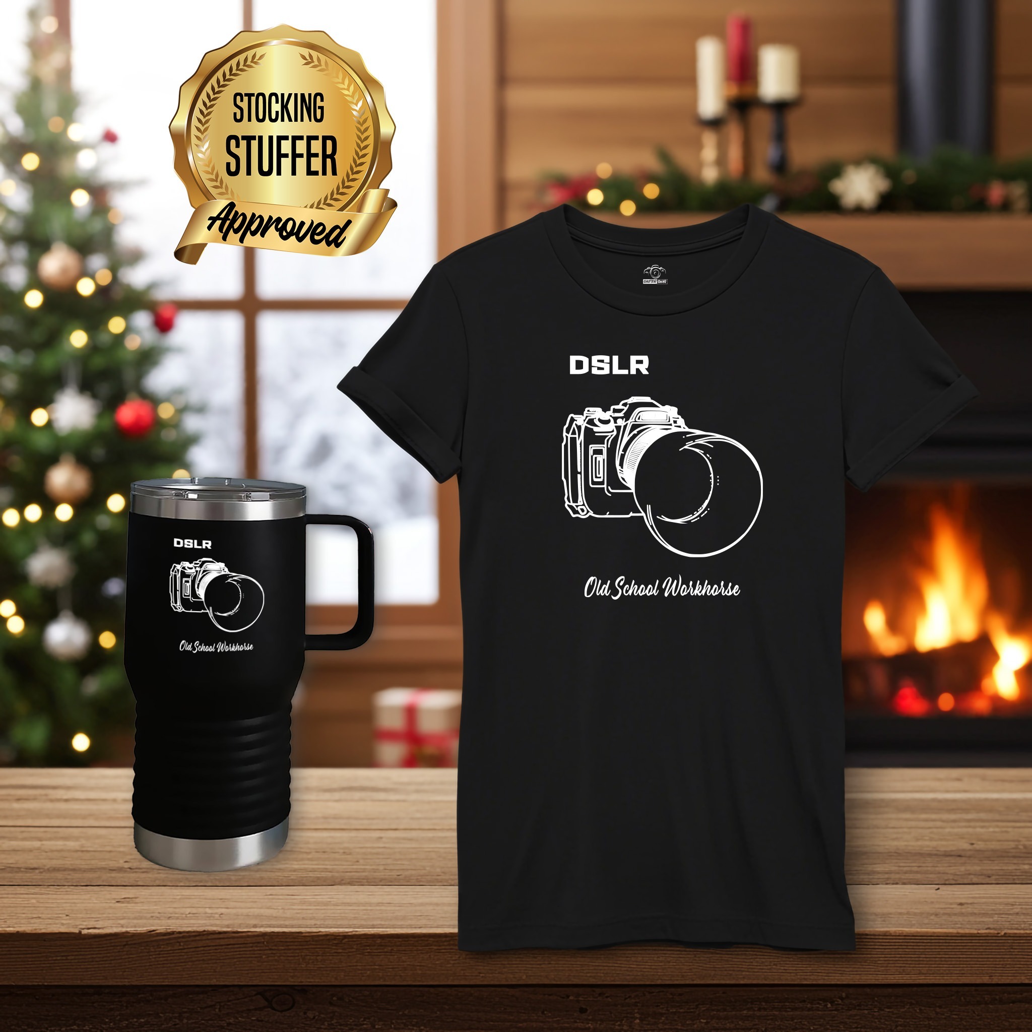 DSLR black t-shirt with travel mug Christmas Stocking Stuffer Approved Black t-shirt and matching travel mug with a white DSLR camera technical line drawing and the words 'DSLR' above the camera and 'Old School Workhorse' below. These Stocking Stuffer approved items are on a wood table in a festive living room with fireplace.